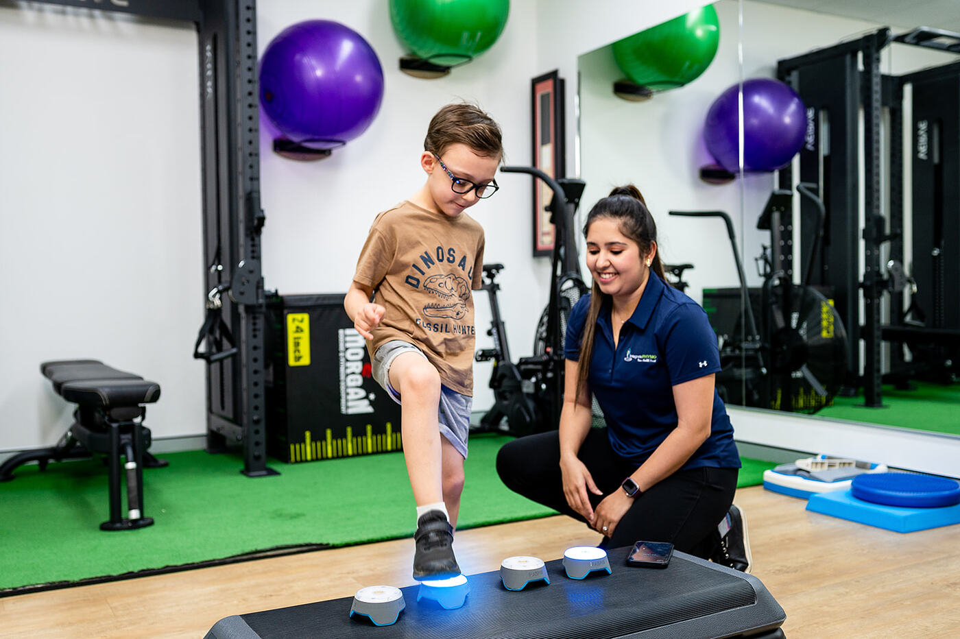 Child stepping onto light-up reaction pods with a physiotherapist